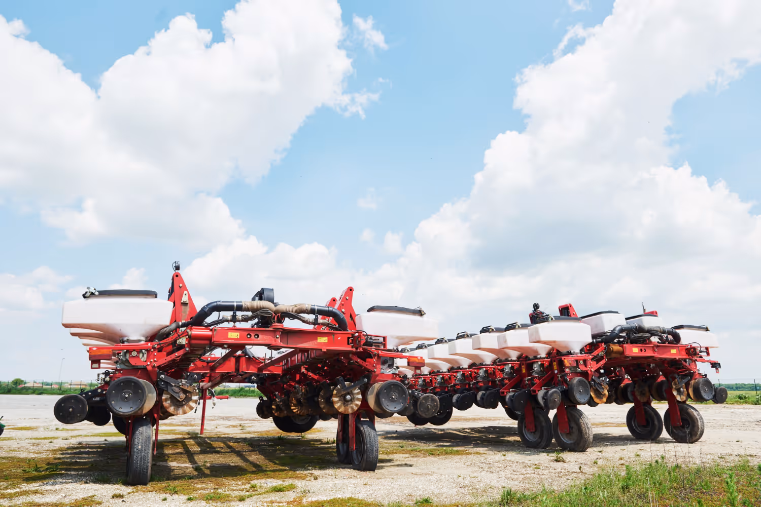 Large red agricultural planter machine with white seed hoppers parked outdoors under a partly cloudy blue sky.